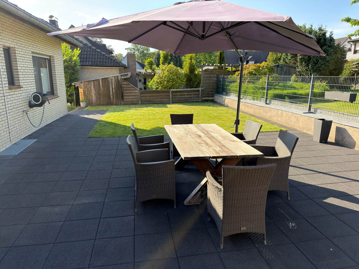 Terrasse mit Esstisch und Sonnenschirm vor ebenem Rasengarten